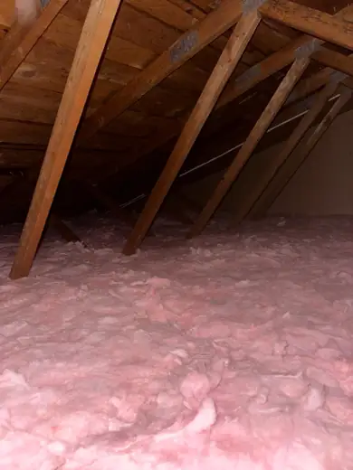 New pink fiberglass insulation filling an attic floor between trusses