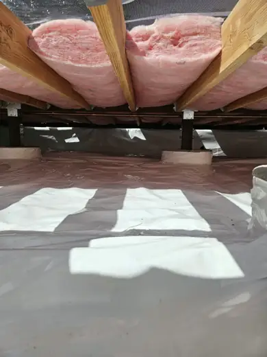 Crawl space with underfloor insulation and a white vapor barrier on the ground
